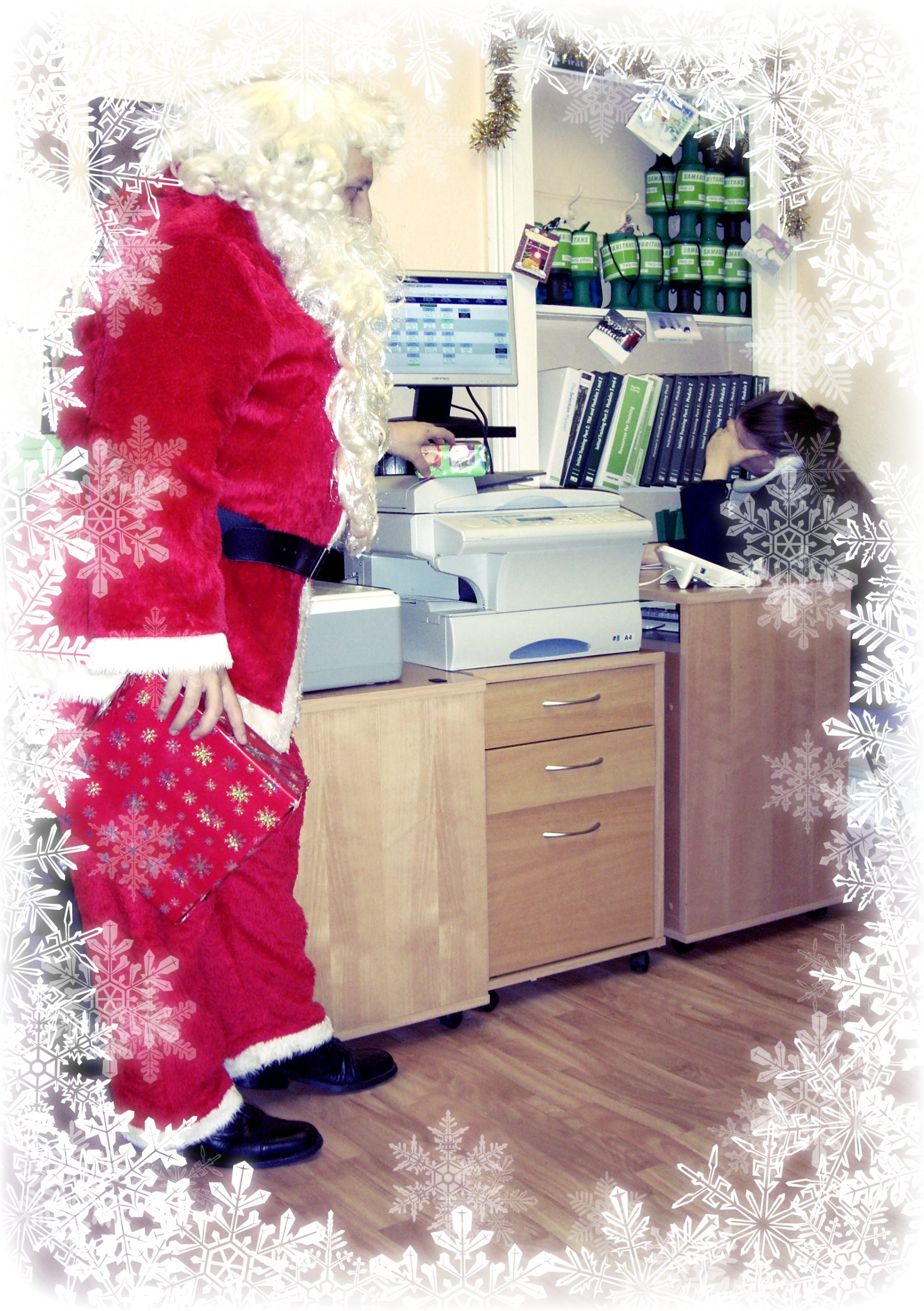 Man in a Father Christmas suit putting a present on the desk next to a volunteer who's on a call