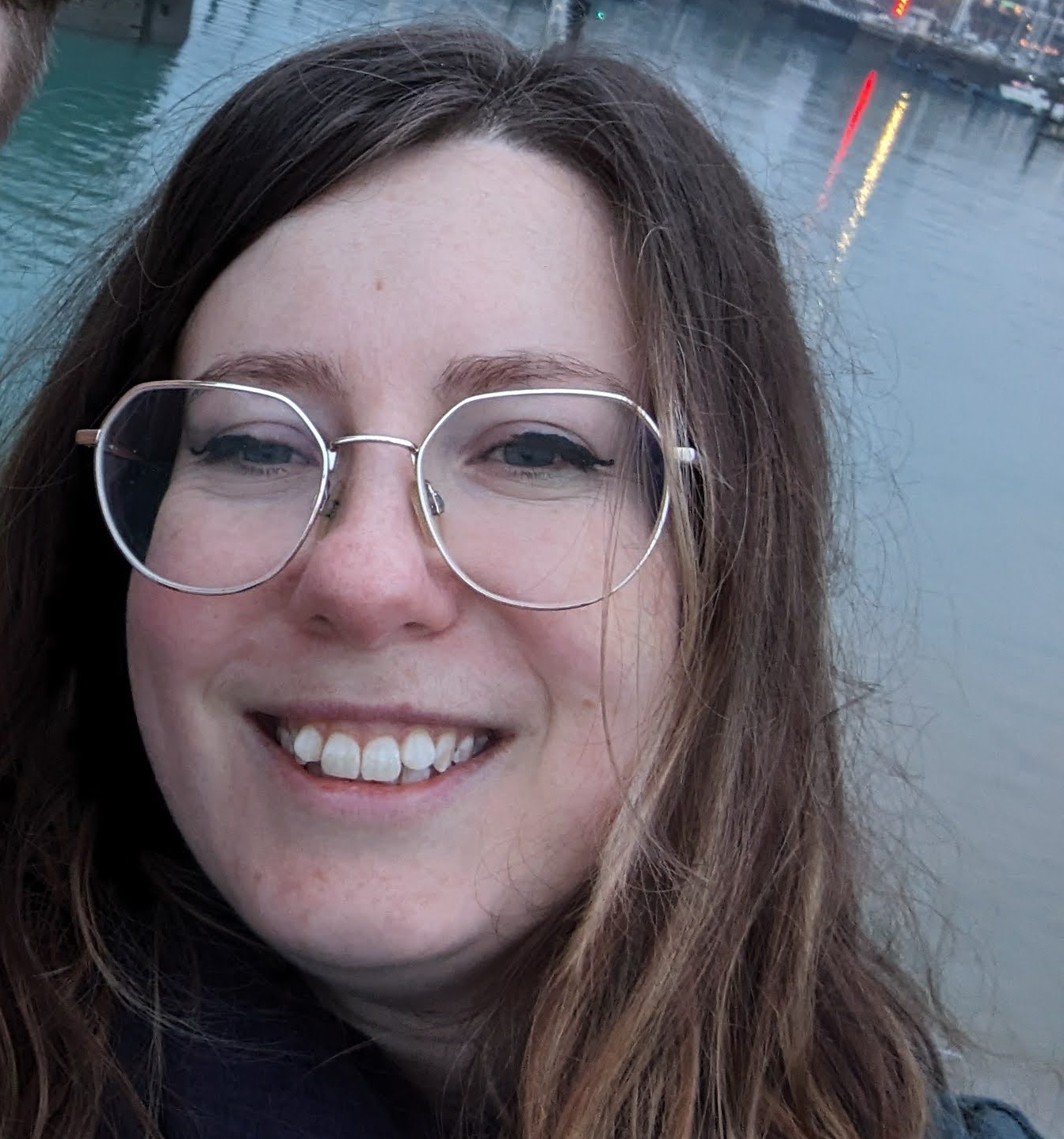 Beverley smiling at camera - weaering round silver glasses, with dark brown hair and pale skin